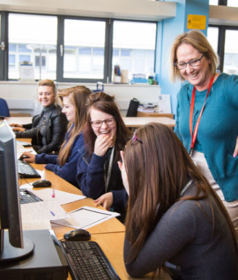 staff member laughing with multiple students sat at computers