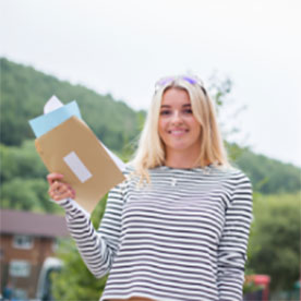 female student outside holing her results with greenery background 