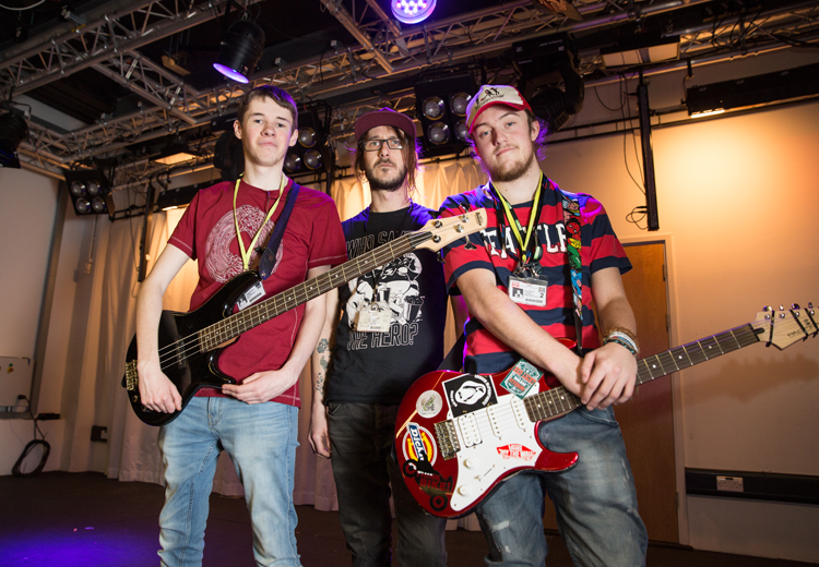 3 male musicians, 2 with guitars on a stage