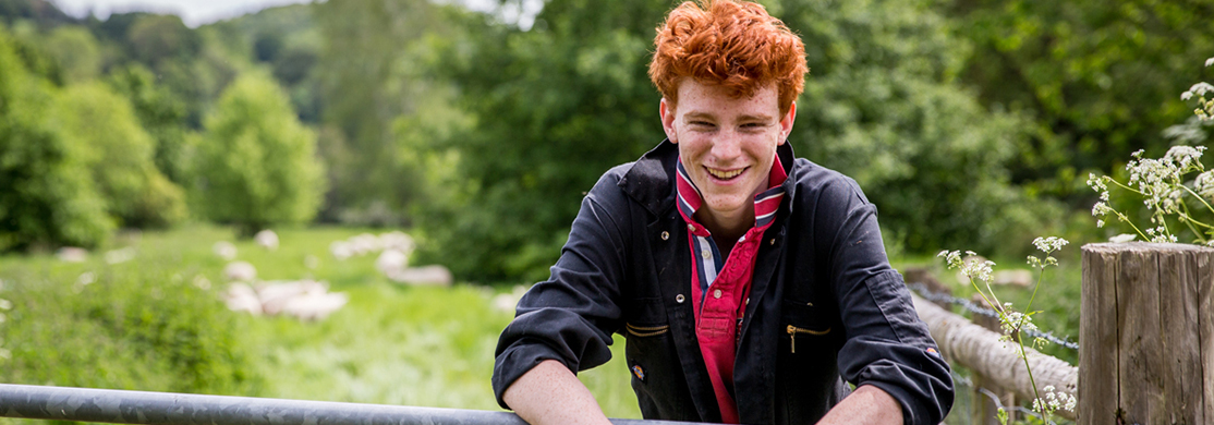 Young man in overalls leaning on a gate