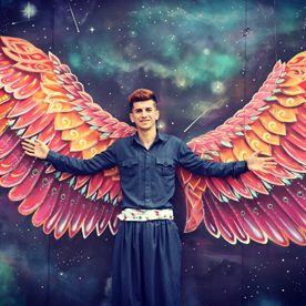 man stood in front of huge coloured wings painted on a wall