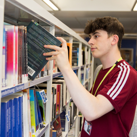 male student taking a book from a shelf in the library