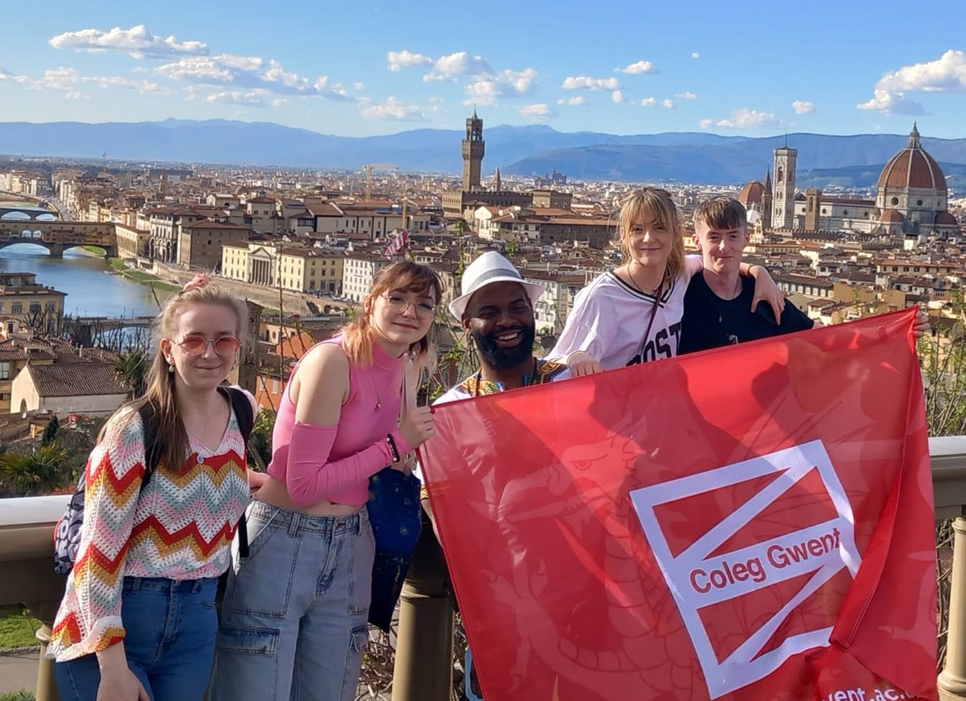 Students smiling holding a Coleg Gwent flag in Italy