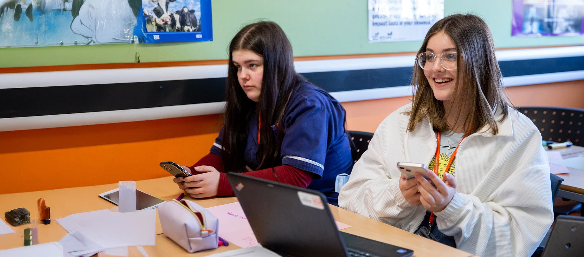 Student holding phone at computer in classroom